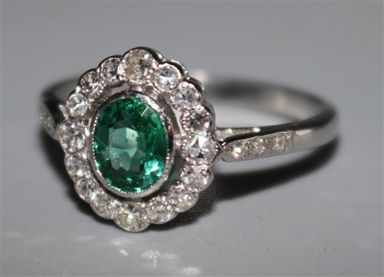 An 18ct white gold, emerald and diamond oval cluster ring with diamond set shoulders, size P.